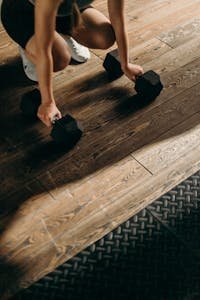 Woman setting up dumbbells in a beginner home gym space with hardwood floors and a simple home strength training setup