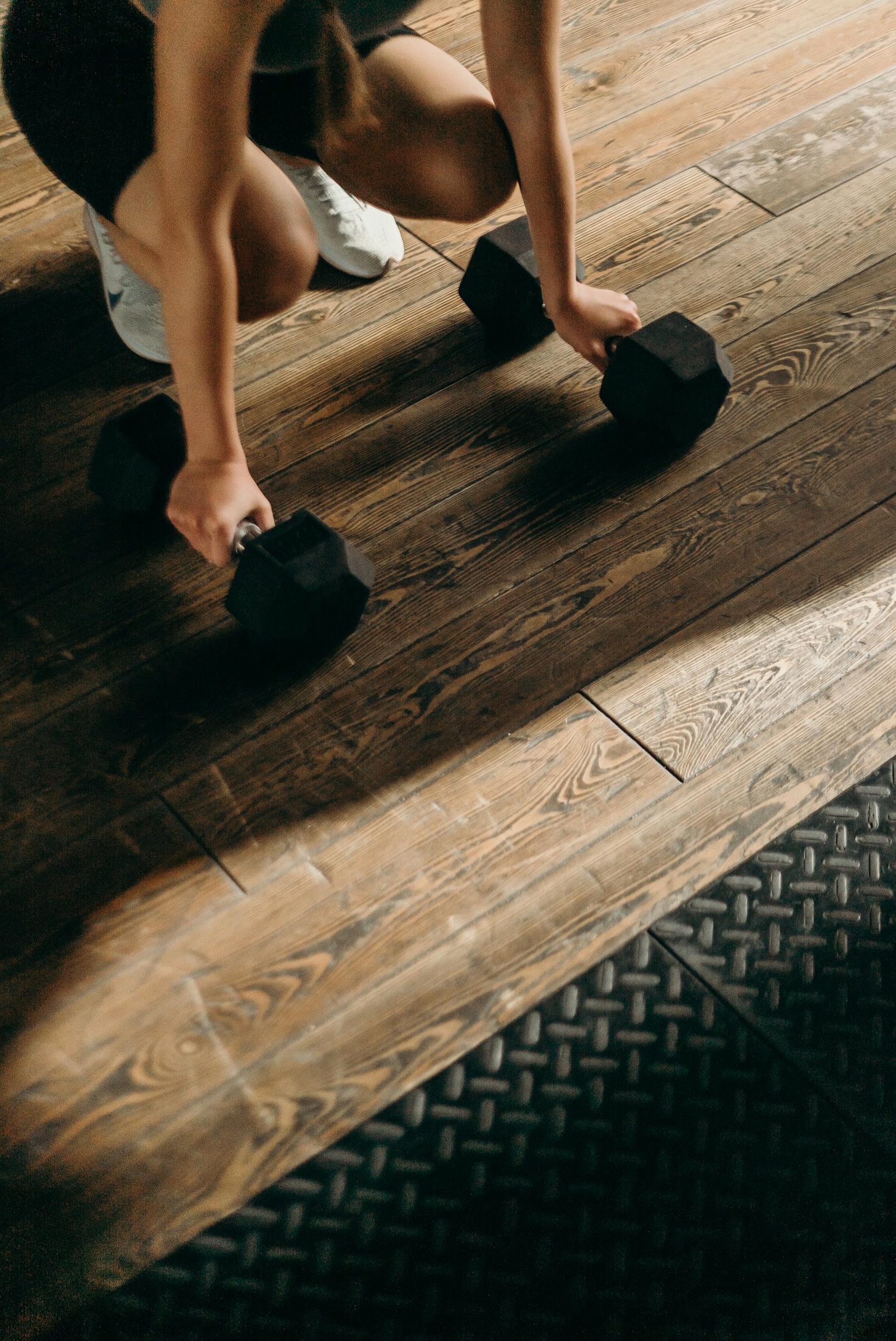 Woman setting up dumbbells in a beginner home gym space with hardwood floors and a simple home strength training setup